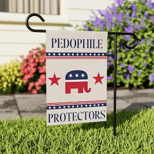 May include: A garden flag with the words "PEDOPHILE PROTECTORS" in navy blue. The flag features a red and blue elephant logo with stars and stripes. The flag is displayed on a black metal stand in a grassy yard.