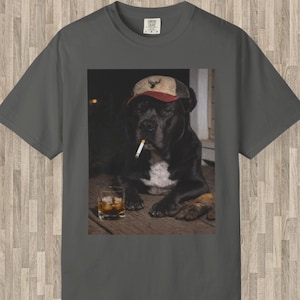 May include: Charcoal grey t-shirt with a graphic of a black dog wearing a cap and smoking a cigarette, with a glass of whiskey. The dog is the central focus, set against a dark background. The cap has a deer emblem.