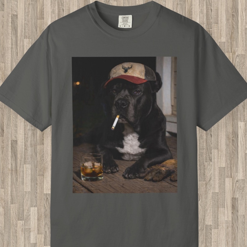 May include: Charcoal grey t-shirt with a graphic of a black dog wearing a cap and smoking a cigarette, with a glass of whiskey. The dog is the central focus, set against a dark background. The cap has a deer emblem.