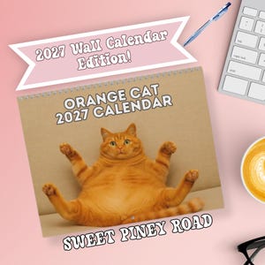 May include: A spiral-bound wall calendar featuring a photograph of an orange cat sitting in a reclined position. The cover text reads 2027 Wall Calendar Edition, Orange Cat 2027 Calendar, and Sweet Piney Road. The calendar is set against a light pink background.