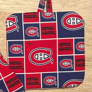 May include: A square, quilted pot holder with a loop for hanging. The design features a repeating pattern of red squares with the Montreal Canadiens logo and text on a blue background. The pot holder is made of fabric.