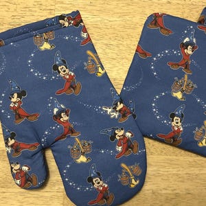 May include: Blue oven mitt and pot holder set featuring a repeating pattern of Mickey Mouse in a sorcerer's outfit. The design includes stars and other magical elements. The oven mitt has a loop for hanging.