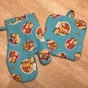 May include: A matching oven mitt and pot holder set. The set is light blue and features a repeating pattern of a cartoon character in a circular design. The word "HERO" is printed on the pot holder. The oven mitt has a loop for hanging.