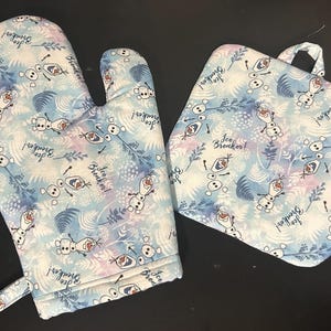 May include: Oven mitt and pot holder set featuring a light blue and white pattern with Olaf the snowman and the text "Ice Breaker!". The set is made of fabric and is designed for kitchen use.