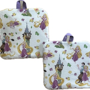 May include: Two white, square-shaped oven mitts with a purple handle. The mitts feature a repeating pattern of a princess with long blonde hair, a tower, and other characters. The design includes purple, yellow, and green accents.