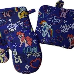 May include: A blue oven mitt and pot holder set. The set features a repeating pattern of cartoon ponies, stars, hearts, and the words "Love", "Star", and "Show Pony". The mitt has a loop for hanging.