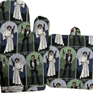 May include: A Star Wars-themed oven mitt, oven glove, and pot holder set. The set features a repeating pattern of Princess Leia and Han Solo in a stained-glass window design, with a color palette of white, black, green, and gray.