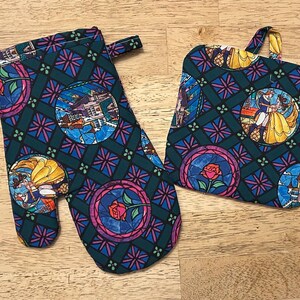 May include: A matching oven mitt and pot holder set. The set features a stained glass design with images of a castle, a rose, and characters in a teal, blue, pink, and yellow color scheme.