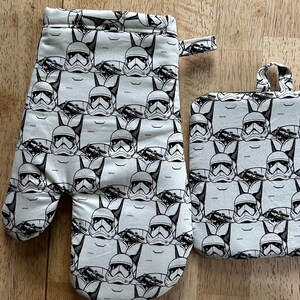 May include: A white oven mitt and pot holder set with a repeating black and white Stormtrooper helmet pattern. The oven mitt has a loop for hanging. The pot holder has a loop for hanging.