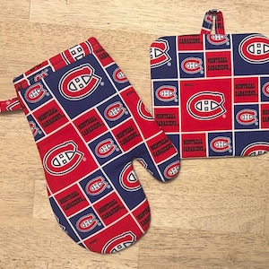 May include: A red, white, and blue oven mitt and pot holder set. The set features a repeating pattern of the Montreal Canadiens logo and team name. The oven mitt has a loop for hanging. The pot holder is square with a loop.