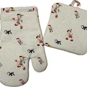 May include: Oven mitt and pot holder set featuring a light blue striped pattern with cartoon illustrations of Pinocchio, Figaro the cat, and Jiminy Cricket. The oven mitt has a loop for hanging. The pot holder is square with a hanging loop.