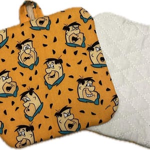 May include: A set of two orange and white pot holders with a cartoon pattern of a man with a bow tie. The pot holders are quilted and have a white backing.