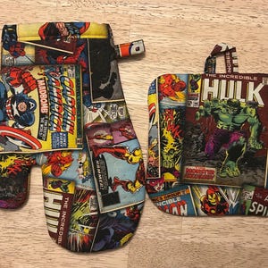 May include: A Marvel Comics-themed oven mitt and pot holder set. The mitt features Captain America and Iron Man comic book panels. The pot holder displays the Incredible Hulk. Both items have a colorful collage design with comic book text.