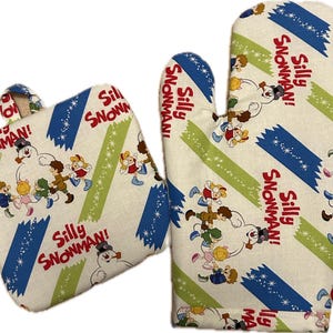 May include: A set of two oven mitts with a white background and blue and green stripes. The mitts feature a cartoon snowman and children with the text "Silly Snowman!" repeated throughout.