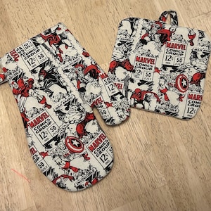 May include: A Marvel Comics-themed kitchen set featuring an oven mitt, pot holder, and small mitt. The set is white with a comic book print in red and black, including comic book panels and text. The oven mitt measures approximately 13 inches long.