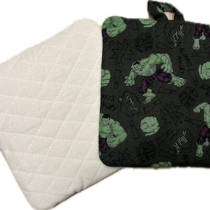 May include: A set of two green and black pot holders. One pot holder is plain white with a quilted pattern. The other pot holder has a repeating pattern of the Hulk character with the text "Always Angry" and "Hulk Smash".