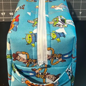 Puede incluir: Un neceser rectangular azul claro con cremallera blanca y un peque&ntilde;o bolsillo. La bolsa est&aacute; decorada con un patr&oacute;n repetido de personajes de dibujos animados, incluyendo Woody, Buzz Lightyear y los Little Green Men. La bolsa est&aacute; hecha de una tela resistente.