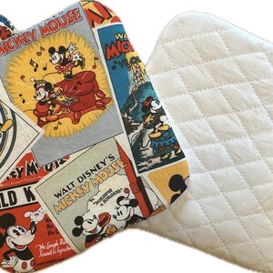 May include: A quilted oven mitt and pot holder set. The oven mitt features a vintage Mickey Mouse print with red, yellow, and blue accents. The pot holder is white with a diamond pattern.