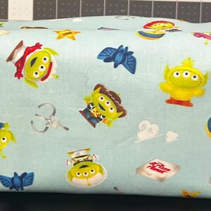 Peut inclure: Une trousse de maquillage rectangulaire bleu clair avec un motif r&eacute;p&eacute;t&eacute; de personnages de Toy Story. Le sac comprend des images d'aliens, de Woody, de Buzz Lightyear et d'autres personnages. Il a une petite poign&eacute;e sur le c&ocirc;t&eacute;.
