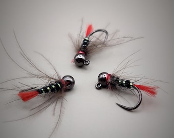 May include: Three black and green fly fishing lures with red accents and black beads. The lures have a feathered tail and are tied on a hook.