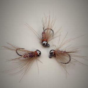 May include: Three brown and purple fly fishing lures with silver beads and hooks.