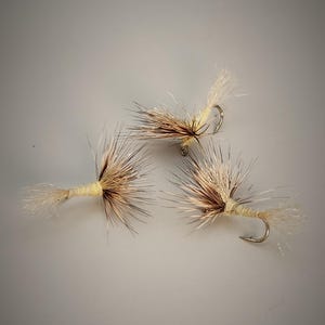 May include: Three tan and brown fly fishing lures with white feathers and a gold hook.