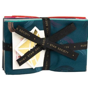 Peut inclure: Un lot de carrés de tissu turquoise avec un motif arc-en-ciel et des accents dorés. Le tissu est noué avec un ruban noir et un autocollant doré qui dit "Ruby Star Society".