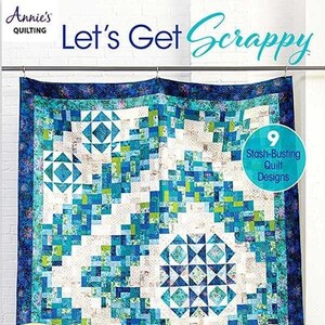 Könnte beinhalten: Ein Buch mit dem Titel "Let's Get Scrappy" von Annie's Quilting, das eine farbenfrohe Quiltdecke aus blauem, grünem und weißem Stoff zeigt. Die Quiltdecke hängt an einer weißen Backsteinwand. Der Buchumschlag enthält auch den Text "9 Stash-Busting Quilt Designs".