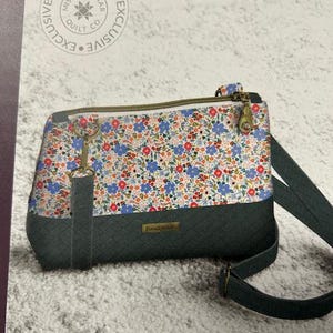 May include: A floral print crossbody bag with a dark green quilted bottom and strap. The bag features a zipper closure and gold-toned hardware. The top portion of the bag has a pattern of blue, red, and white flowers.