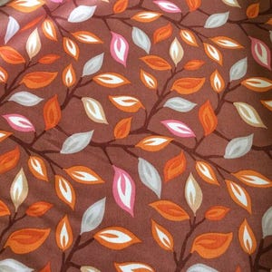 May include: A brown fabric with a repeating pattern of orange, pink, and white leaves. The leaves are stylized and have a simple design.
