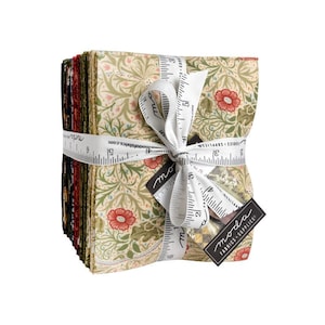 May include: A bundle of fabric squares tied with a white ribbon printed with measurements in centimetres. The fabric features a floral pattern in cream, red, and green. A black tag with the text "moda FABRICS SUPPLIES" is attached.