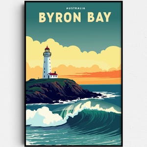 May include: A framed art print featuring a coastal scene of Byron Bay, Australia. The artwork depicts a white lighthouse on a rocky cliff, with a large ocean wave in the foreground. The sky transitions from teal to orange, with the text "BYRON BAY" at the top.