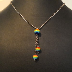 May include: A silver chain necklace with three rainbow-coloured beads. The beads are round and have a striped pattern.