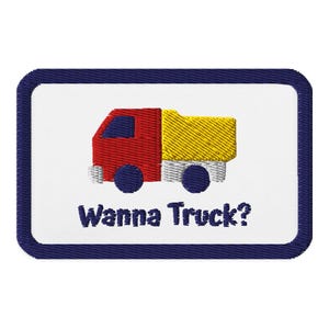 May include: Embroidered patch featuring a red and yellow truck with blue wheels. The patch has a white background with the text "Wanna Truck?" in blue, framed by a navy blue border.