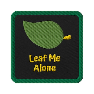 May include: Embroidered patch with a green leaf design and the text "Leaf Me Alone" in yellow. The patch has a black background and a green border. The leaf is detailed with textured stitching.