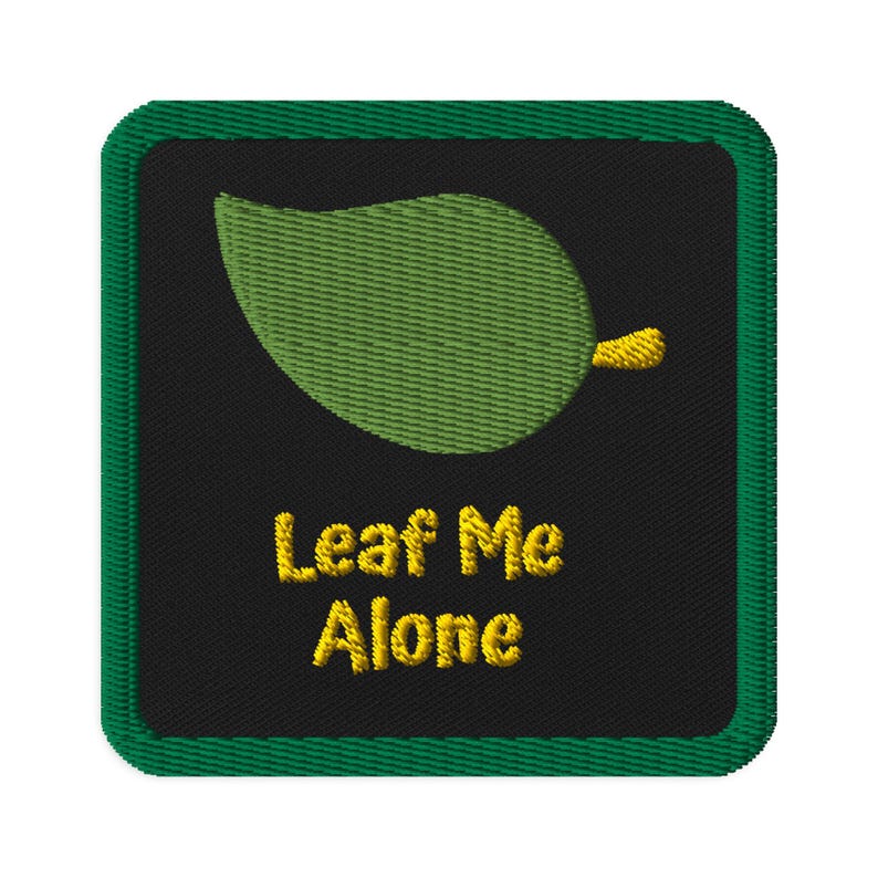 May include: Embroidered patch with a green leaf design and the text "Leaf Me Alone" in yellow. The patch has a black background and a green border. The leaf is detailed with textured stitching.