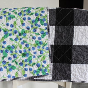 May include: A reversible quilt with a white background featuring a blue and green blueberry pattern on one side and a black and white checked pattern on the other side.