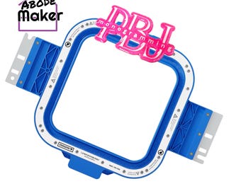 以下が含まれることがあります： 青と白の正方形の刺繍枠で、DBJの文字が入ったピンクのグリッターモノグラムアタッチメントが付いています。枠の側面には金属製の取り付けブラケットがあり、縁には警告ラベルが印刷されています。