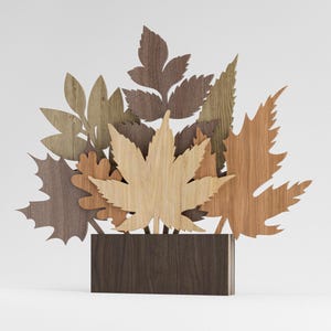 Op de afbeelding: Houten bladersculptuur met verschillende bladvormen en kleuren, waaronder esdoorn- en eikenbladeren. De bladeren zijn gerangschikt in een boeketstijl en geplaatst in een donkerbruine rechthoekige basis. De sculptuur is gemaakt van hout en heeft een natuurlijk, rustiek uiterlijk.