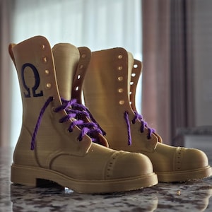 May include: A pair of tan-colored boots with purple laces. The boots have a classic lace-up design with multiple eyelets and a small heel. A purple Omega symbol is on the side of one boot.