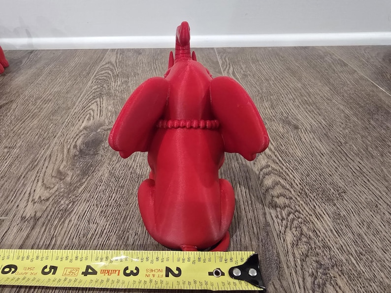 May include: A bright red elephant figurine, viewed from the back, with large ears and a detailed trunk. The elephant is sitting, and a measuring tape is in the foreground. The figurine is approximately 3 inches long.