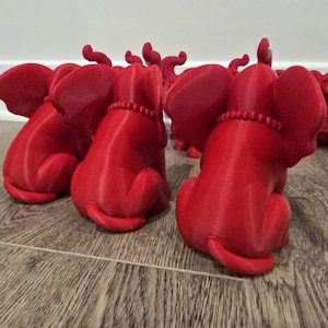 May include: A collection of red elephant figurines, each in a seated position with their trunks raised. The elephants have detailed features, including large ears and beaded necklaces. The figurines are arranged on a wooden surface.