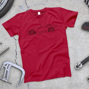 May include: Red t-shirt with a black outline of a convertible car on the front.