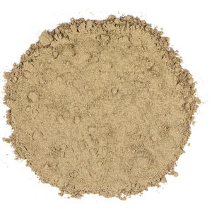 Op de afbeelding: Een hoop fijn, lichtbruin poeder tegen een witte achtergrond. Het poeder heeft een licht getextureerd uiterlijk, met kleine korrels zichtbaar. De algemene vorm is ruwweg cirkelvormig, met enkele ongelijke randen. De kleur is een gedempte, aardse tint.