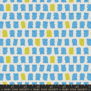 May include: A light grey fabric featuring a repeating pattern of small blue and lime green gummy bear shapes. A black ruler at the bottom edge displays the text RUBY STAR SOCIETY, indicating a measurement scale of 7 inches across the fabric.