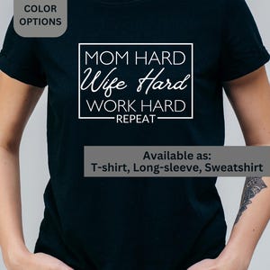 May include: Black t-shirt with the text "MOM HARD, Wife Hard, WORK HARD, REPEAT" in a white, rectangular design. The shirt is available as a t-shirt, long-sleeve, and sweatshirt. Additional color options are available.