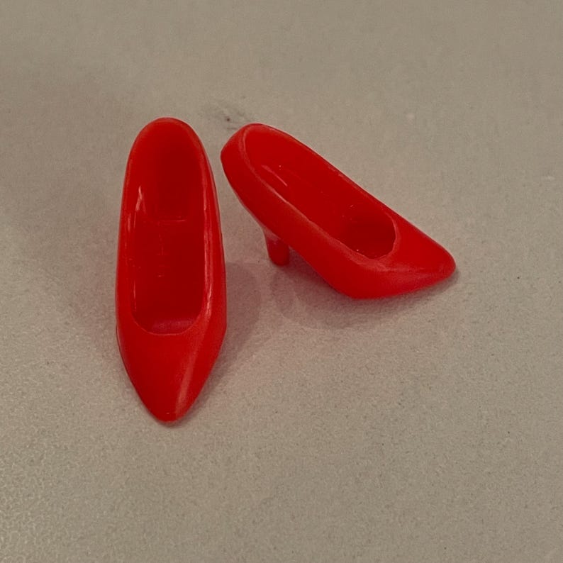 May include: A pair of red high-heeled shoes. The shoes are made of plastic and have a pointed toe.