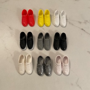 May include: A collection of ten pairs of miniature sneakers in various colours, including black, white, red, yellow, and grey. The sneakers are arranged in two rows of five pairs each.