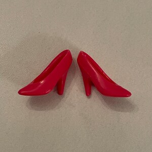 May include: A pair of bright red high-heeled shoes. The shoes are made of plastic and have a simple, classic design.