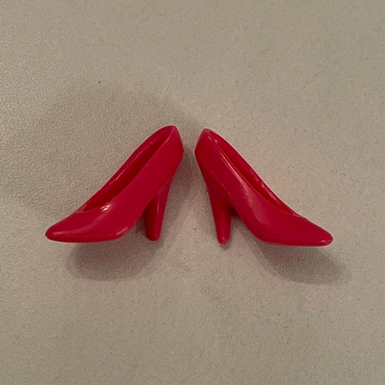May include: A pair of bright red high-heeled shoes. The shoes are made of plastic and have a simple, classic design.